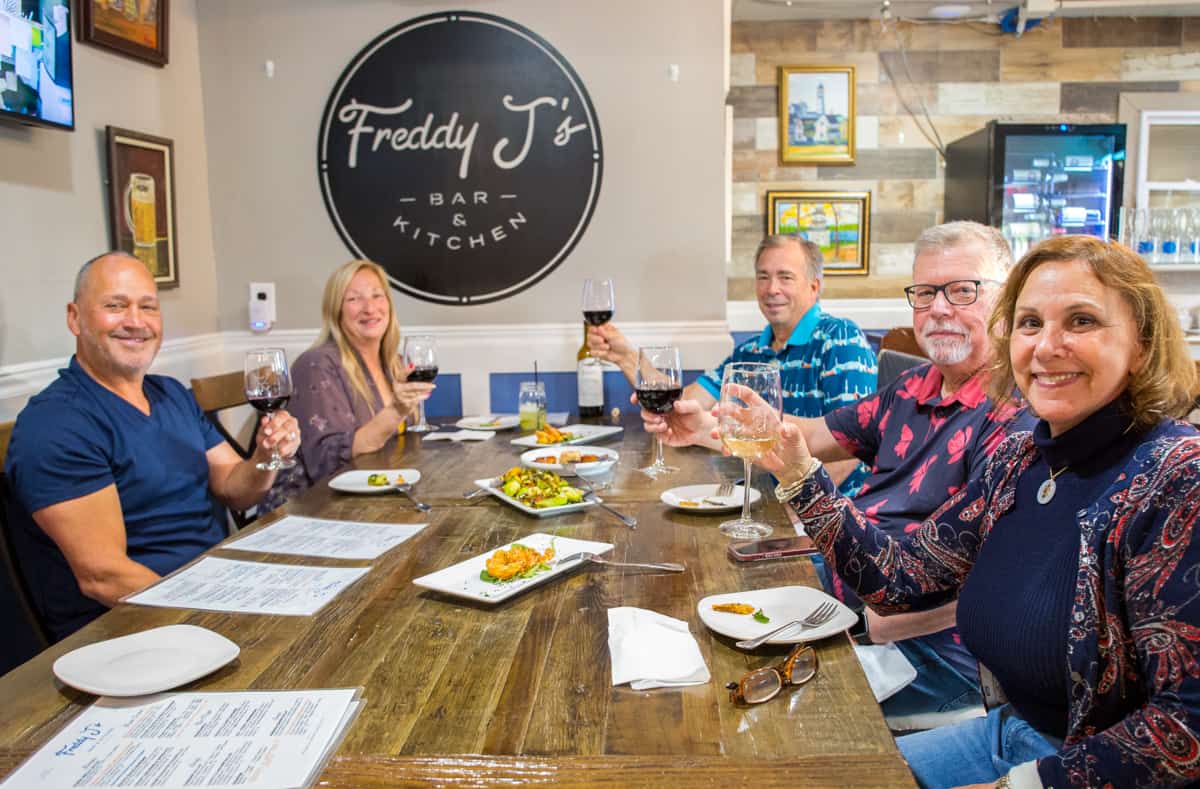 A party of five toasting their wine at Freddy J's Bar & Kitchen while enjoying appetizers.